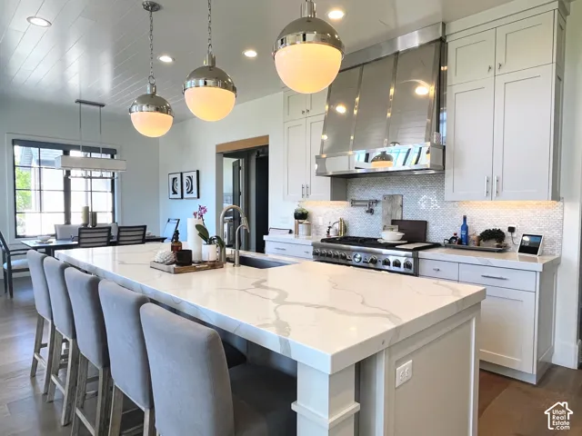 Gourmet kitchen featuring a substantial island with stone countertops, a professional-grade range, a tile backsplash, custom cabinetry, and wood-finish flooring