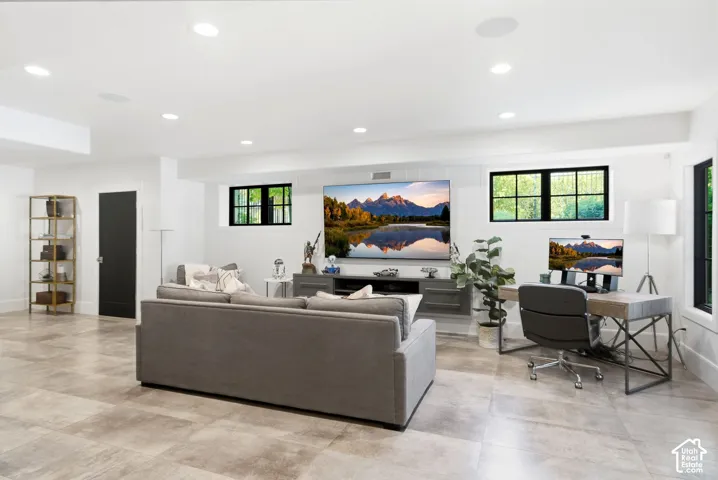 Spacious entertainment area featuring recessed lighting, light-toned tile flooring, and multiple windows with dark framing