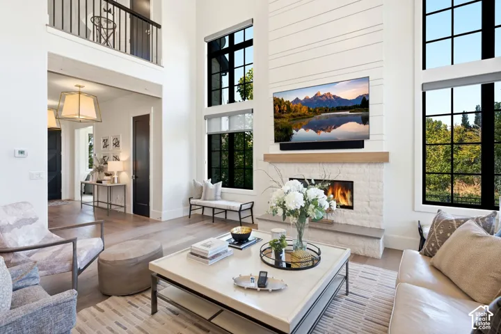 Double-height living area featuring a shiplap accent wall, a fireplace with a stone surround and wood mantel, and large black-framed windows