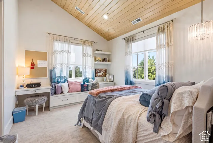 Vaulted wood-paneled ceiling accentuates this carpeted room featuring a built-in window seat with storage, white desk cabinetry, and a tiered chandelier