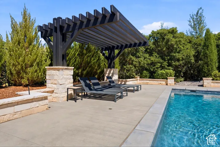 Black wood pergola with stone pillars, concrete pool deck, and a rectangular swimming pool with light blue water