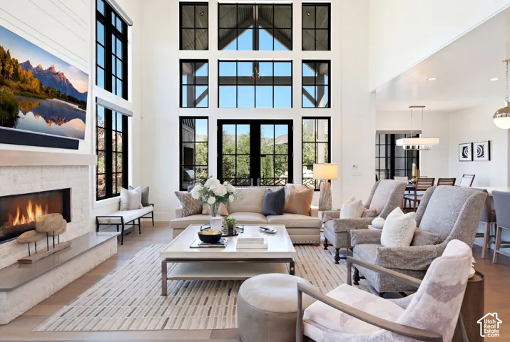 Two-story living area featuring a full-height window wall with dark-framed panes, a built-in linear fireplace with a stone surround, high ceilings, wood-finish flooring, and a recessed dining area with pendant lighting