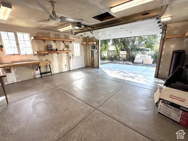 Attached ceiling fan, two fluorescent light fixtures, two windows, built-in shelving, and a concrete floor