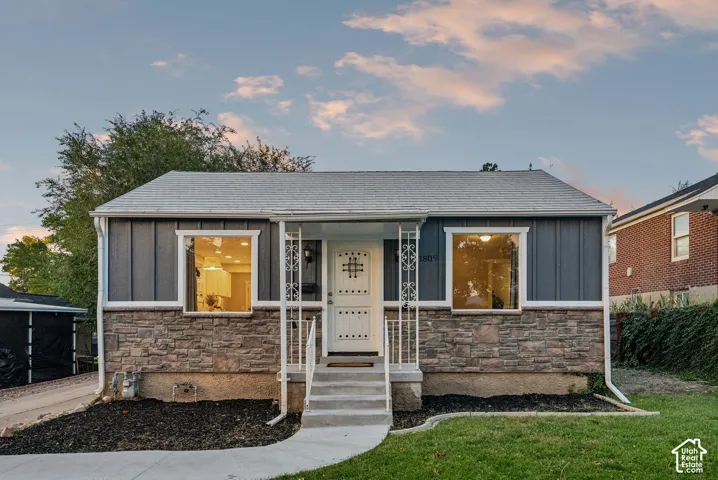 Charming brick and stone-clad ranch featuring a freshly updated exterior with modern siding, large picture windows flooding the interior with natural light, a welcoming covered entry with decorative columns, and a manicured front lawn with mature landscap