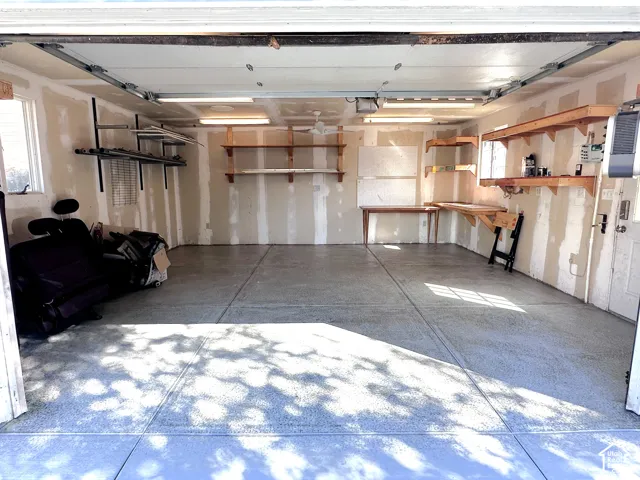 Concrete flooring, extensive built-in shelving, built-in workbench, overhead lighting, and a single window
