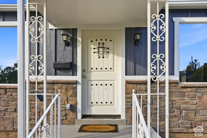 Decorative wrought iron porch columns and railing, stone veneer foundation, board and batten siding, and an ornate front door with a speakeasy grille