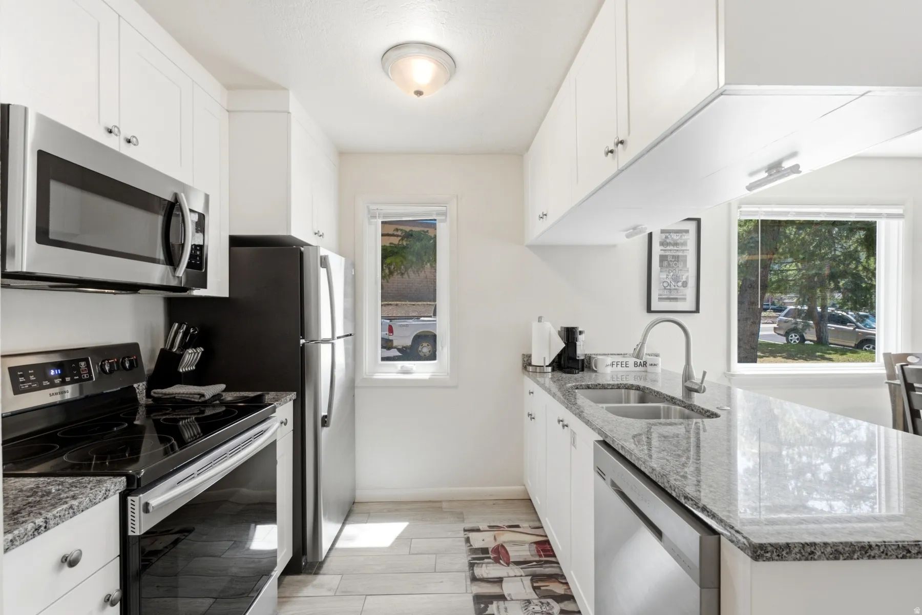 Contemporary kitchen featuring white cabinetry, stainless steel appliances, granite countertops, and light wood-finish flooring
