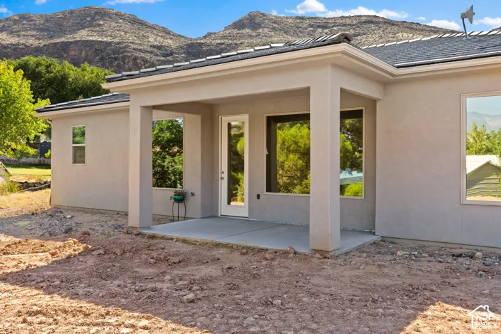 Rear elevation featuring a covered concrete patio, stucco exterior, multiple windows, and a glass-paneled door