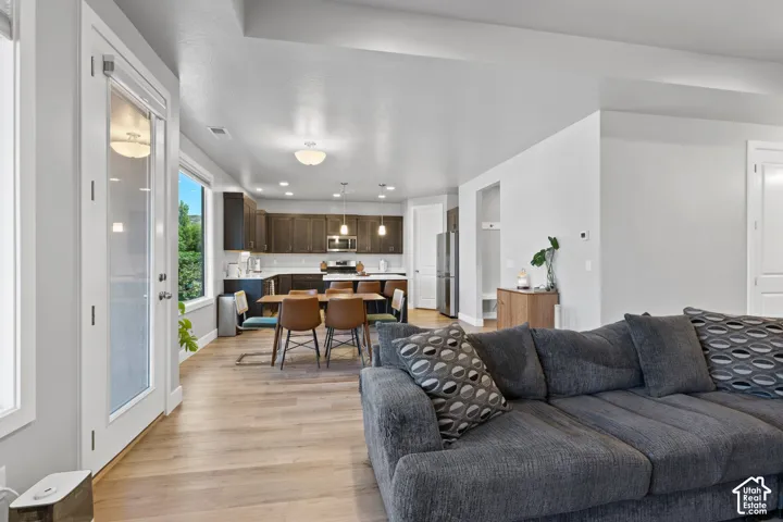 Open-concept living space featuring wood-finish flooring, a kitchen with dark cabinetry, white countertops, and stainless steel appliances, and a dining area with a modern light fixture