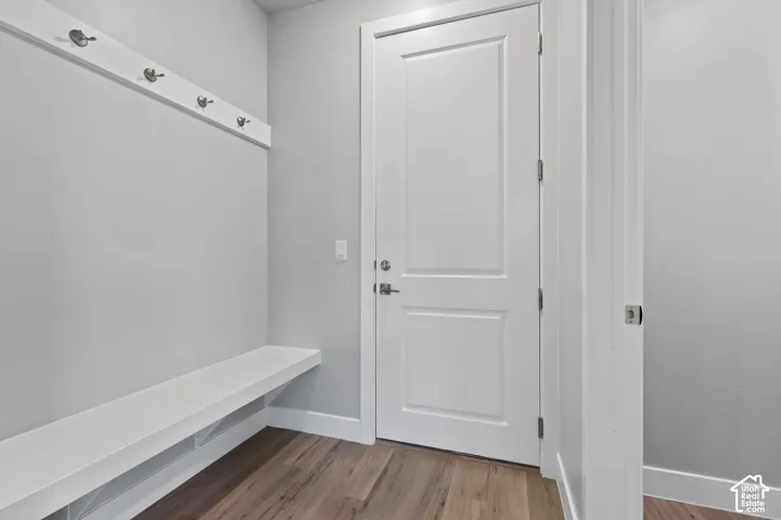Entryway mudroom featuring a built-in bench, wall-mounted coat rack with five hooks, wood-finish flooring, and a white paneled door with brushed nickel hardware