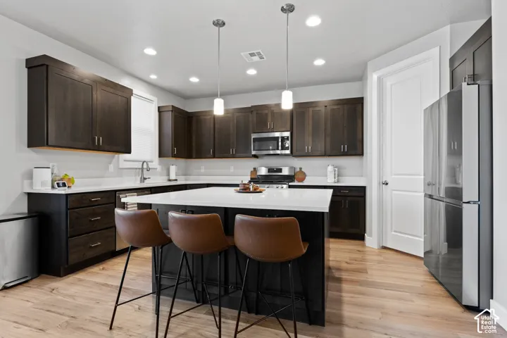 Spacious kitchen featuring dark wood cabinetry, light countertops, stainless steel appliances, a central island with integrated seating, and wood-finish flooring