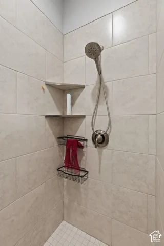 Walk-in shower featuring light-toned large format wall tiling, a handheld shower fixture with a brushed nickel finish, and integrated corner shelving