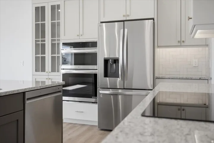 Stainless steel kitchen appliances, granite-style countertops, wood-finish flooring, white shaker-style cabinetry, and subway tile backsplash