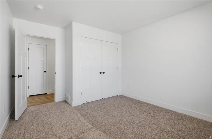 White walls with clean lines, light brown carpet flooring, built-in closet with double doors, white trim, and a white interior door with black hardware
