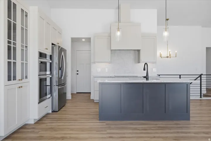 Kitchen featuring a central island with a stone countertop, built-in stainless steel double ovens, wood-finish flooring, and pendant lighting
