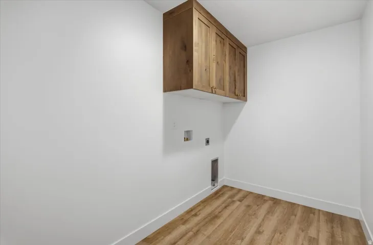 Wood-finish flooring, white baseboards, and overhead wooden cabinetry with brass-toned hardware