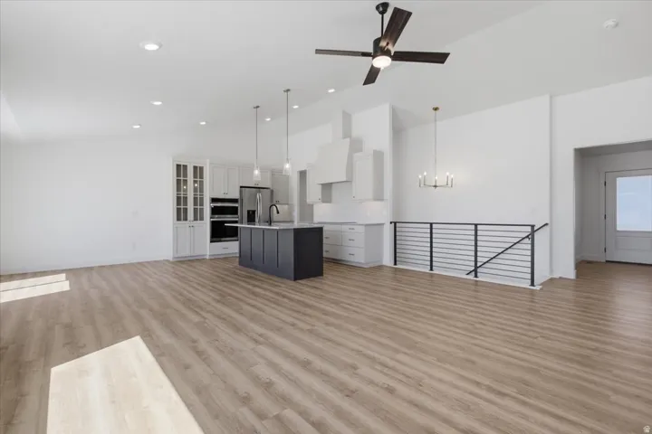 Vaulted ceiling with a ceiling fan, recessed lighting, wood-finish flooring, kitchen island with pendant lighting, and stainless steel appliances