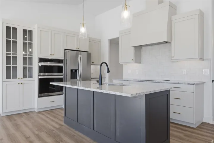 Modern kitchen featuring a central island with a light-toned countertop, stainless steel appliances, light cabinetry with glass-front accents, and wood-finish flooring