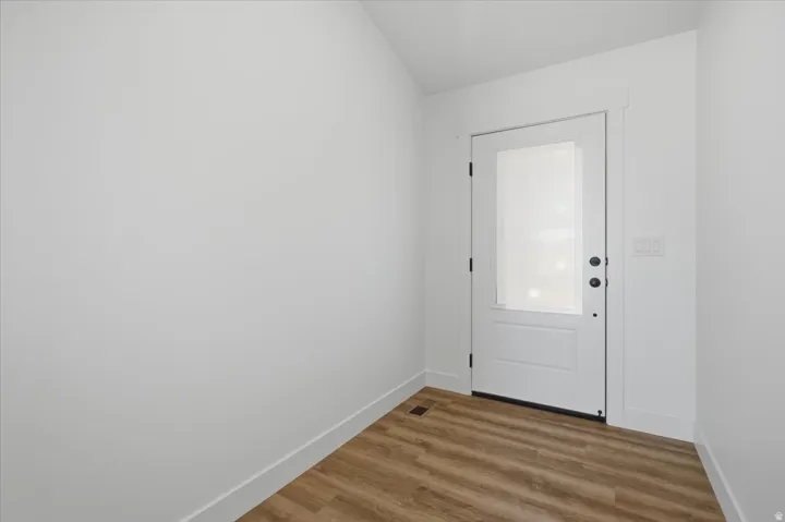 Wood-finish flooring, white door with frosted glass panel, white wall trim, and white walls