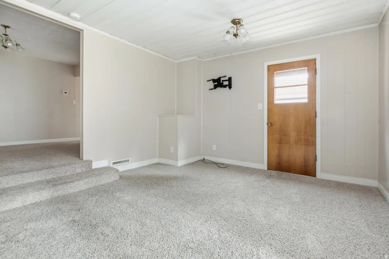 Carpeted interior space featuring light-toned walls, white trim, and a paneled ceiling