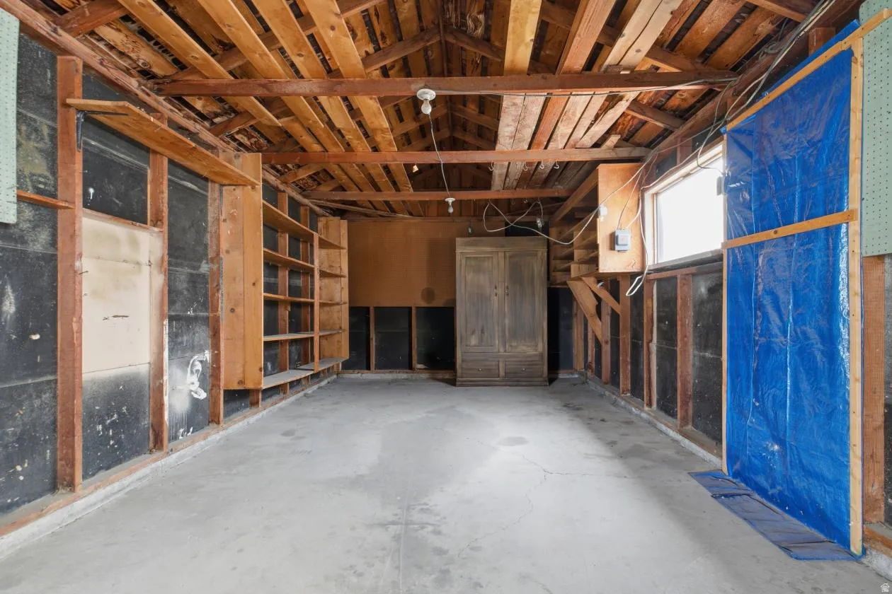 Open storage space with exposed wood beam ceiling, built-in shelving, concrete flooring, and a window for natural light