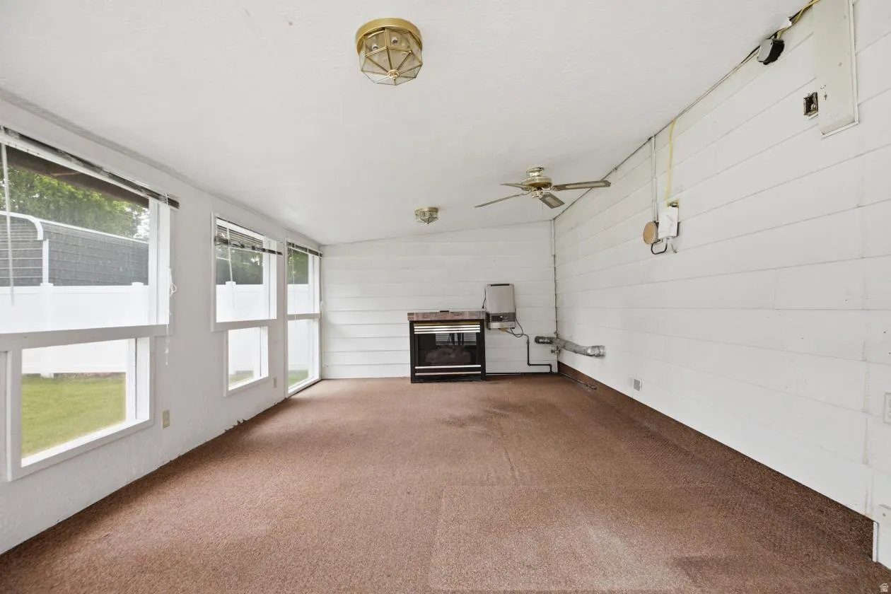 Spacious interior room featuring multiple windows, a ceiling fan, brown carpeting, and a built-in fireplace unit