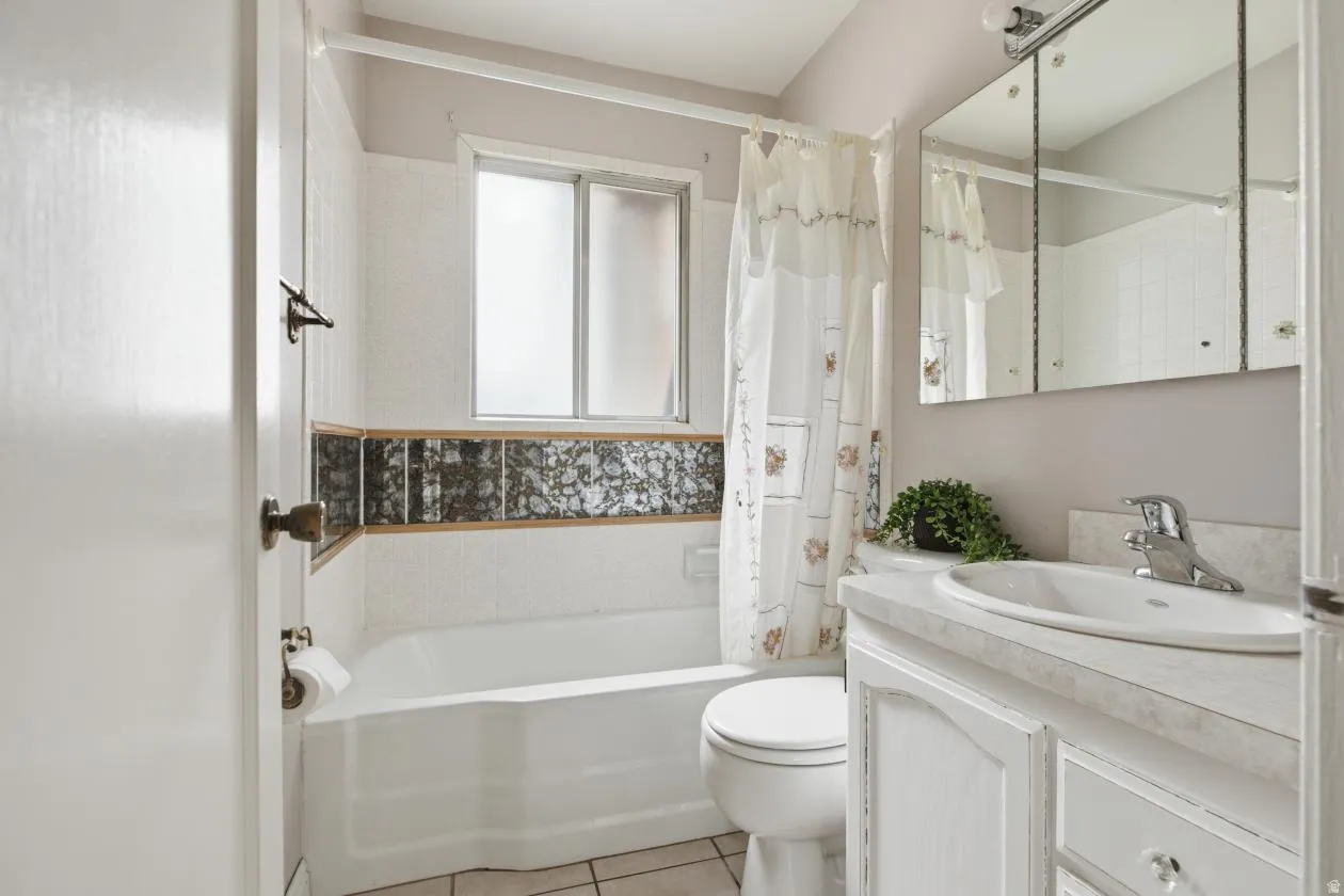Bathroom featuring a full tub, a vanity with an integrated sink, a three-panel mirrored medicine cabinet, a frosted window, and floor tiling