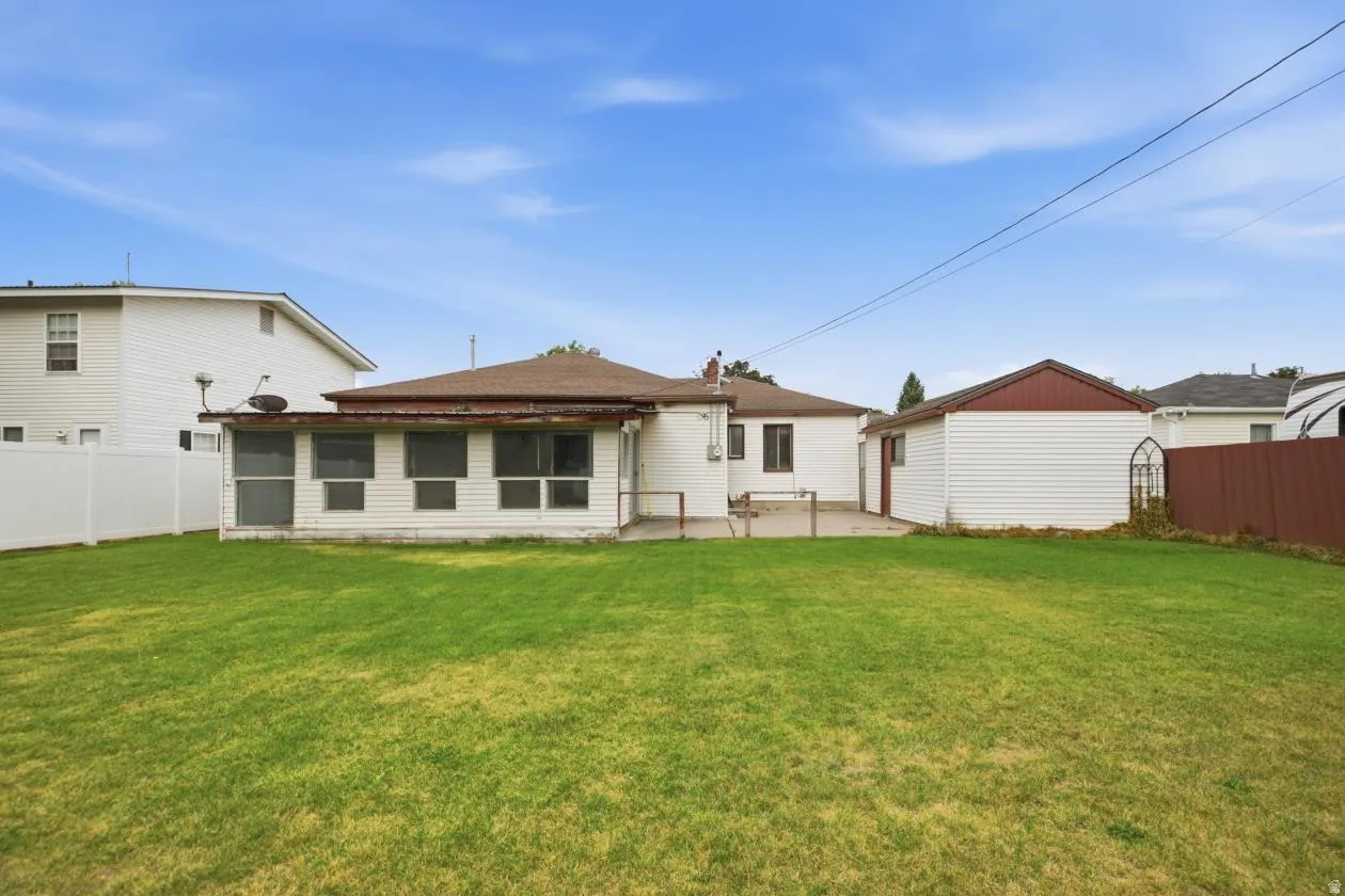Expansive green lawn with a white vinyl fence and a detached garage featuring white siding and a brown roof trim