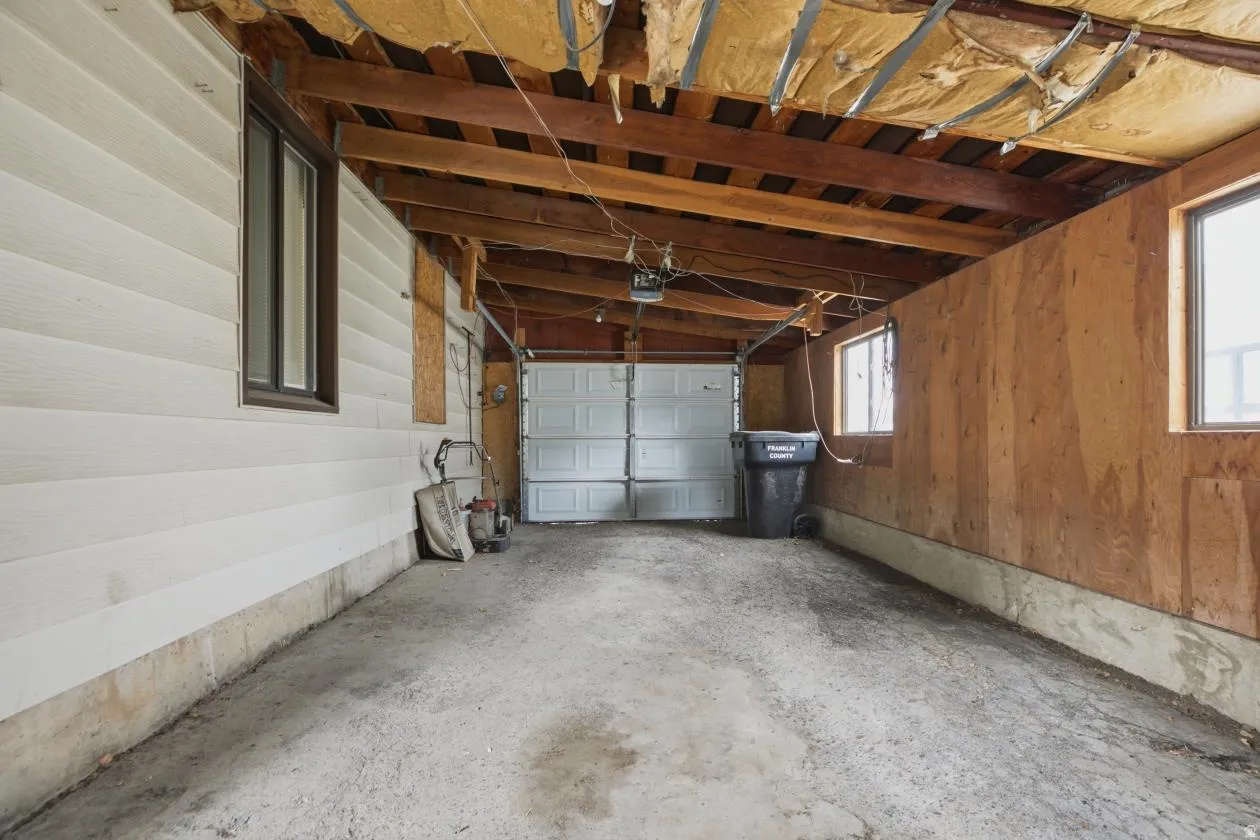 Spacious covered parking area featuring a concrete floor, exposed wood beams, and a white paneled garage door