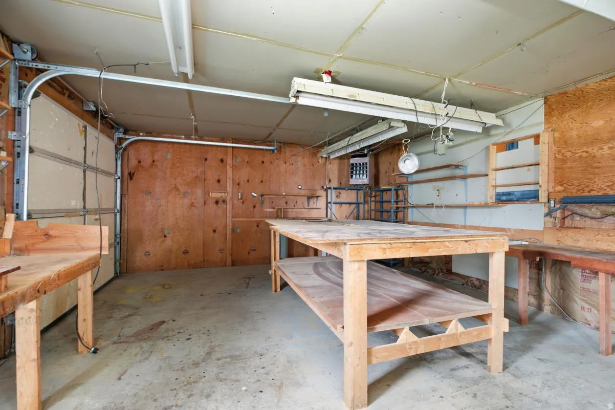 Utility space featuring a concrete floor, exposed plywood walls, multiple built-in shelving units, and overhead fluorescent lighting