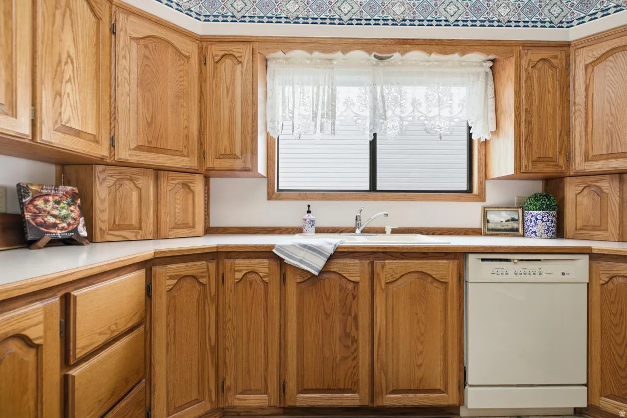 Kitchen featuring extensive wood cabinetry, light-toned countertops, an integrated sink, and a built-in dishwasher