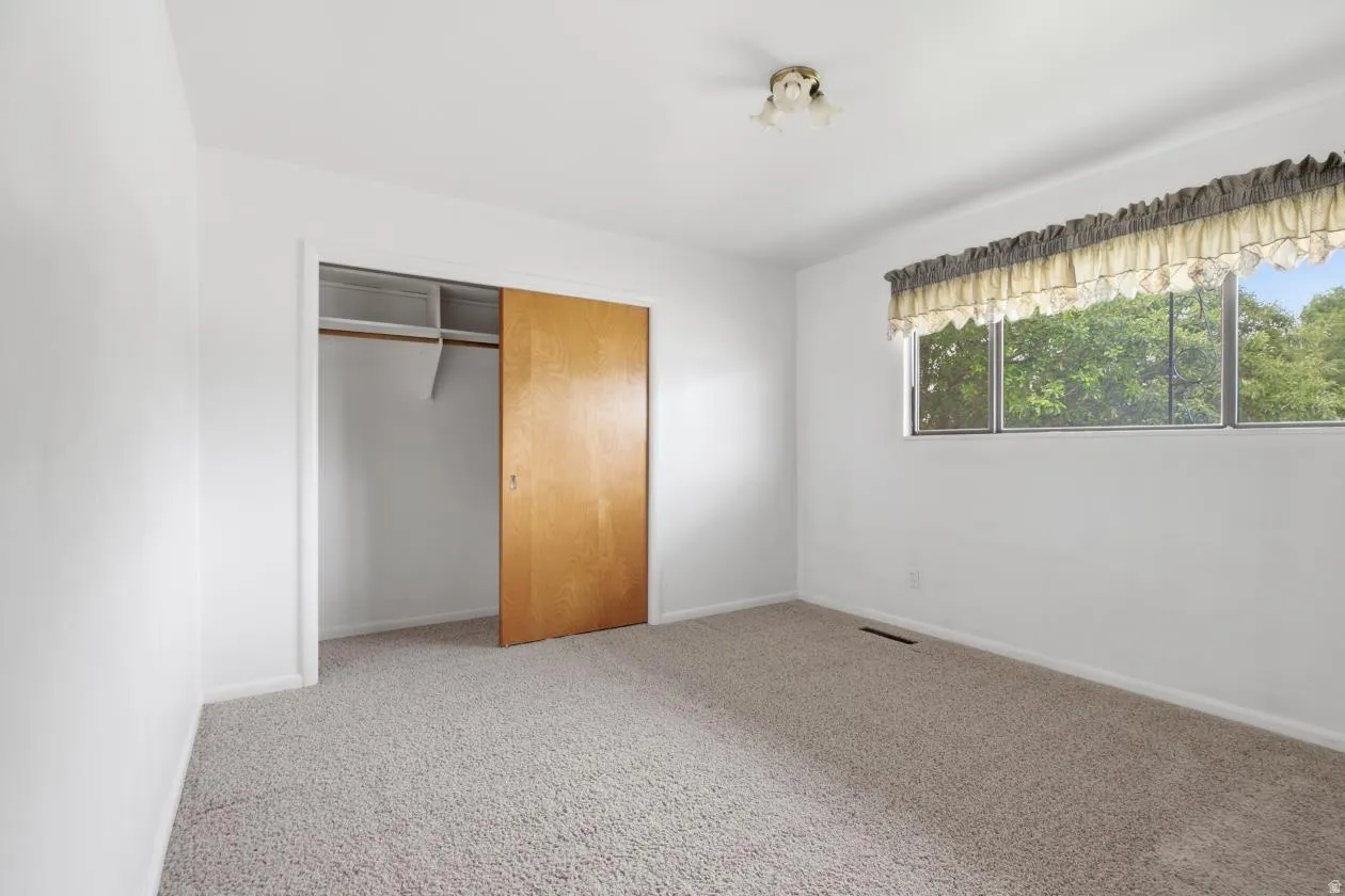 Bedroom featuring light-colored carpeting, white painted walls, a flush-mount ceiling light fixture, and a window overlooking exterior greenery