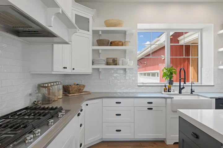 Kitchen featuring white cabinetry, subway tile backsplash, a built-in gas range with stainless steel hood, an apron-front sink with a black gooseneck faucet, and light-colored countertops