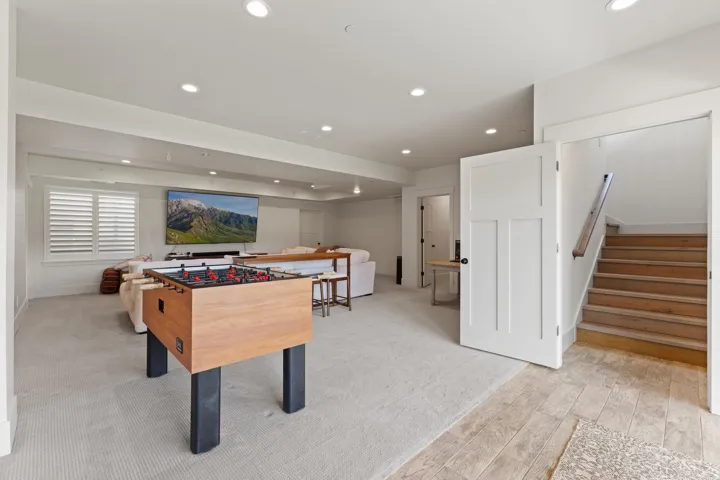 Lower-level recreational space featuring recessed lighting, plush carpeting, and a large wall-mounted screen