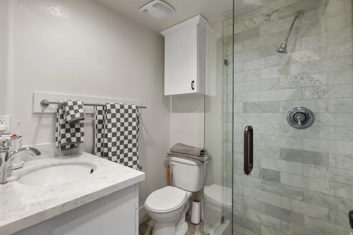 Bathroom featuring a glass-enclosed shower with subway tile, a vanity with a white countertop and undermount sink, a wall-mounted storage cabinet, and brushed nickel fixtures
