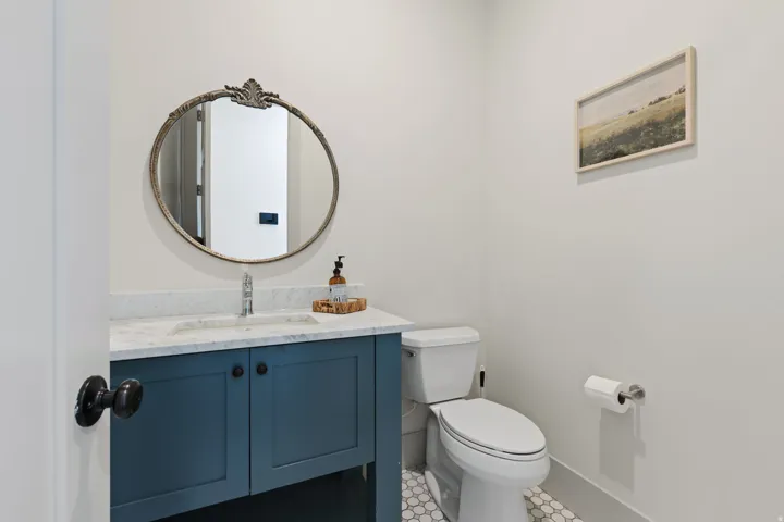 Powder room featuring a blue vanity with a white countertop, an oval mirror, and hexagonal tile flooring
