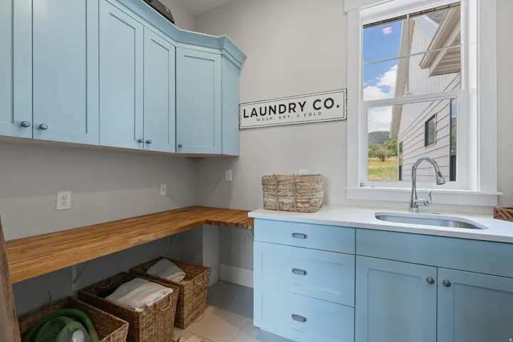 Laundry room featuring light blue cabinetry, a stainless steel sink with a high-arc faucet, white countertops, and a wood-finish folding counter