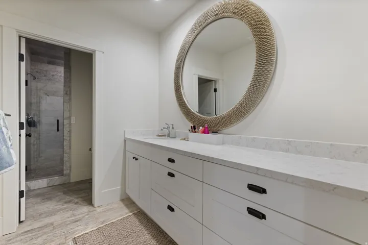 Contemporary bathroom featuring a spacious white vanity with ample counter space, a large round mirror, and a walk-in shower with glass enclosure