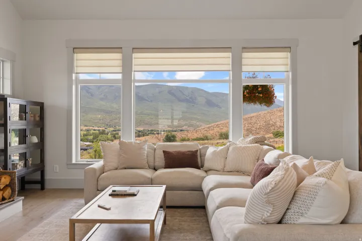 Bright living area featuring a four-panel window array with roller shades, light wood-finish flooring, and a contemporary dark wood display cabinet