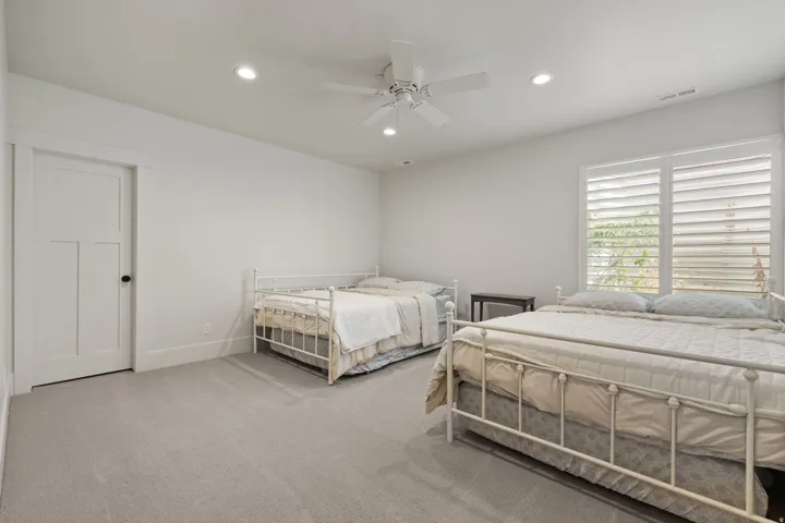 Spacious room featuring light gray carpeting, recessed lighting, a ceiling fan, a paneled door with black hardware, and windows fitted with plantation shutters