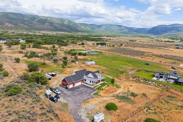 Expansive property featuring a two-story residence with a covered porch, a detached red garage with white garage doors, a paved driveway, and varied terrain, all set against a backdrop of distant mountains