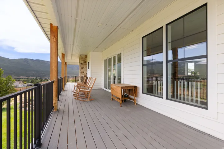 Expansive covered porch featuring gray composite decking, black metal railings, and natural wood support columns