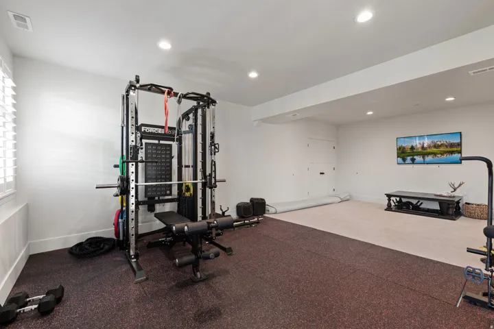 Versatile lower-level space featuring recessed lighting, a dedicated workout area with specialized flooring, and a separate carpeted section