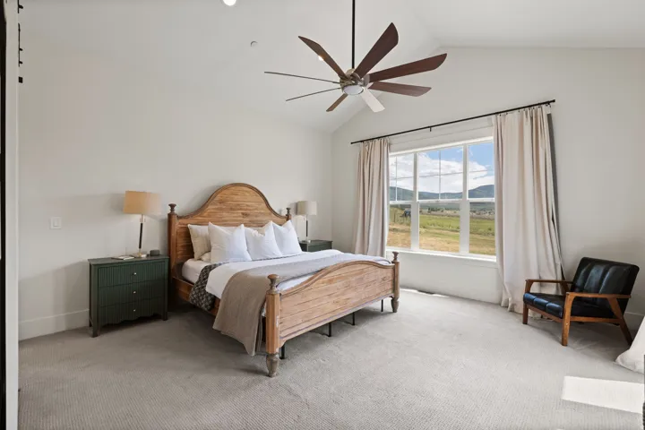 Interior room featuring a vaulted ceiling with a ceiling fan, a large window with a landscape backdrop, and light-toned carpeting