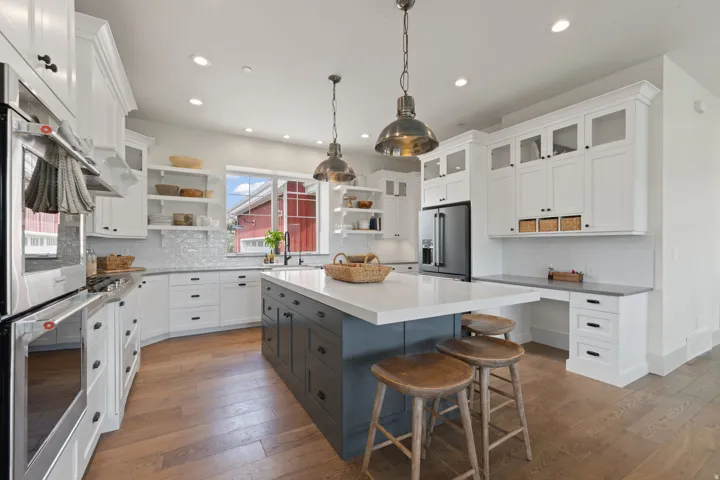 Kitchen featuring a large central island with a light-colored countertop, white cabinetry with black hardware, wood-finish flooring, stainless steel appliances, and built-in desk space