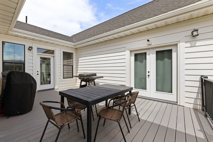 Expansive outdoor deck with gray composite flooring, white siding, and multiple entry points featuring French doors and additional windows