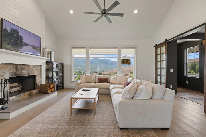Spacious living area featuring a vaulted ceiling, stone-surround fireplace, wood-finish flooring, and multiple large windows