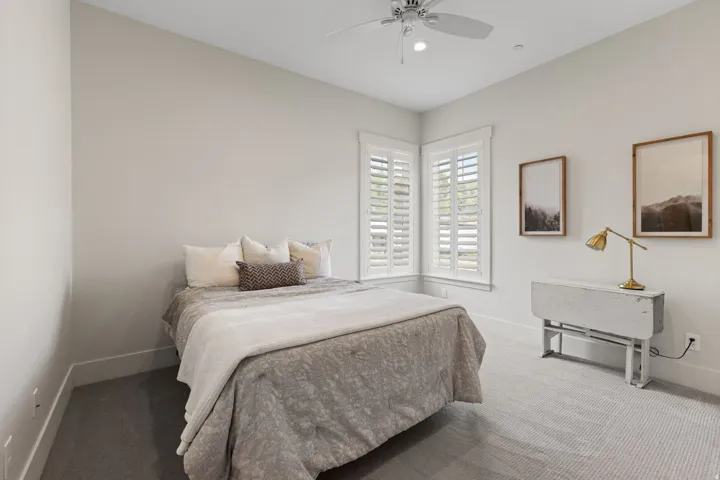 Bedroom featuring dual windows with white plantation shutters, neutral wall tones, and a ceiling fan with integrated lighting