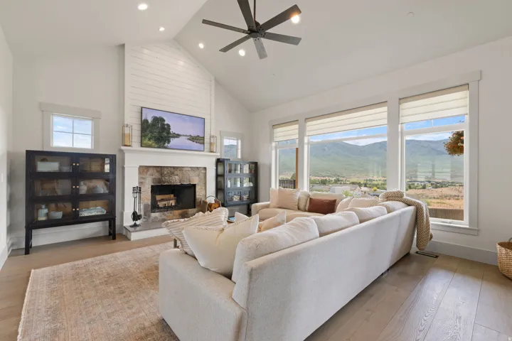 Spacious living area featuring a stone fireplace with a shiplap accent wall, vaulted ceiling with recessed lighting, wood-finish flooring, and expansive windows showcasing mountain scenery