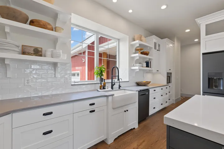 Kitchen featuring white cabinetry with dark hardware, a farmhouse-style sink, light gray countertops, white subway tile backsplash, and wood-finish flooring
